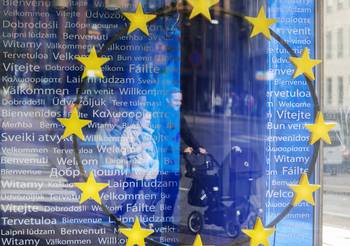 Kuvassa perhe heijastuu rakennuksen ikkunasta, jossa on keltaisia tähtiä.