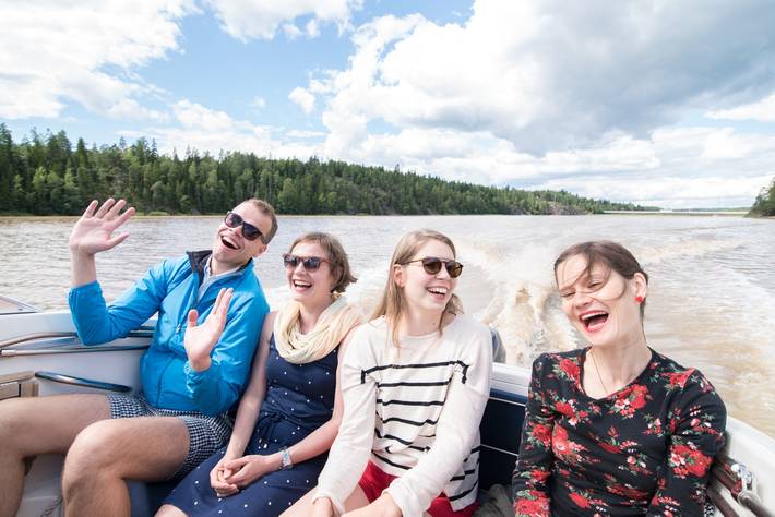 Kuva neljästä iloisesta nuoresta aikuisesta, jotka ovat moottoriveneen kyydissä.