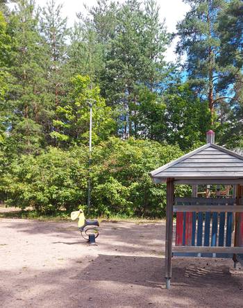 Kuva on Lappeenrannan Mäntylän leikkipaikalta. Kuvassa on leikkipaikan nykyisiä leikkivälineitä ja ympäröivää kasvillisuutta. 